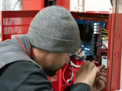 State Fire technician performing low voltage fire alarm system installation in a commercial facility for fire protection and life safety compliance.