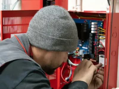 State Fire technician performing low voltage fire alarm system installation in a commercial facility for fire protection and life safety compliance.