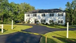A white house with yellow caution tape blocking the driveway after a new asphalt surface and sealcoating service