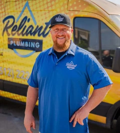 Reliant Plumbing employee posing in uniform in from of a yello work truck