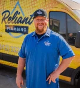 Reliant Plumbing employee posing in uniform in from of a yello work truck