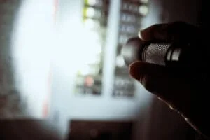 Electrician inspecting residential electrical panel with flashlight during emergency repair.