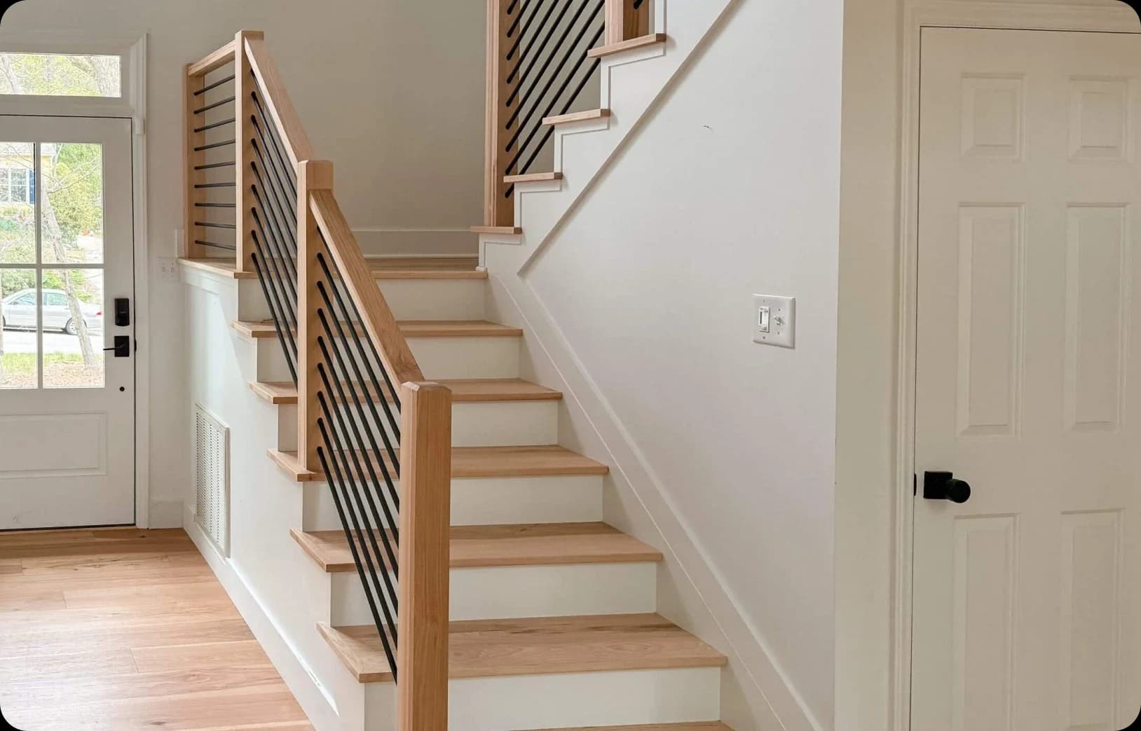 Modern staircase with light wooden steps, minimalist railings, glass door, white walls.