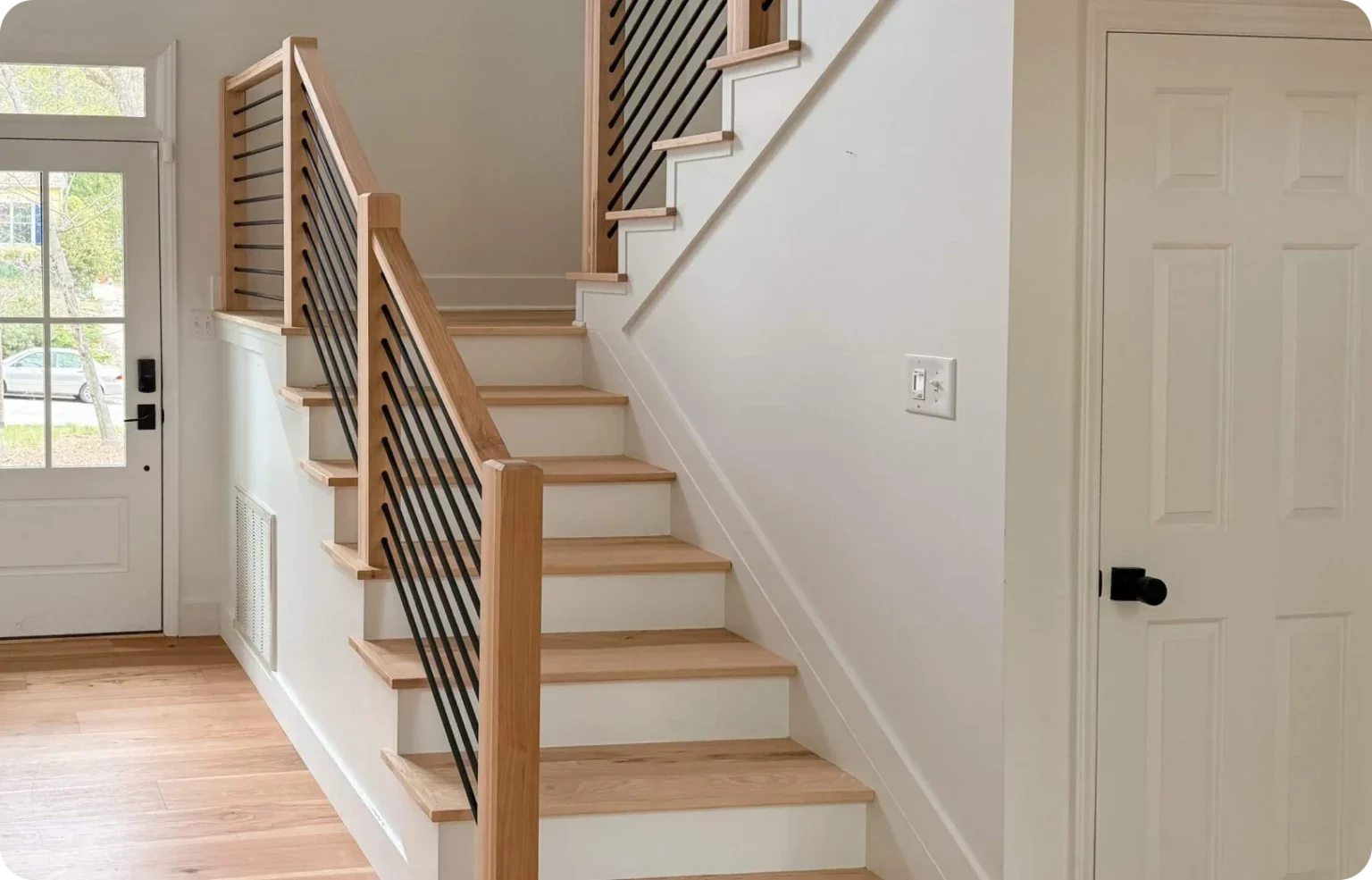 Modern staircase with light wooden steps, minimalist railings, glass door, white walls.