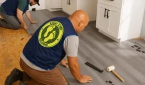 Two workers installing flooring with tools.