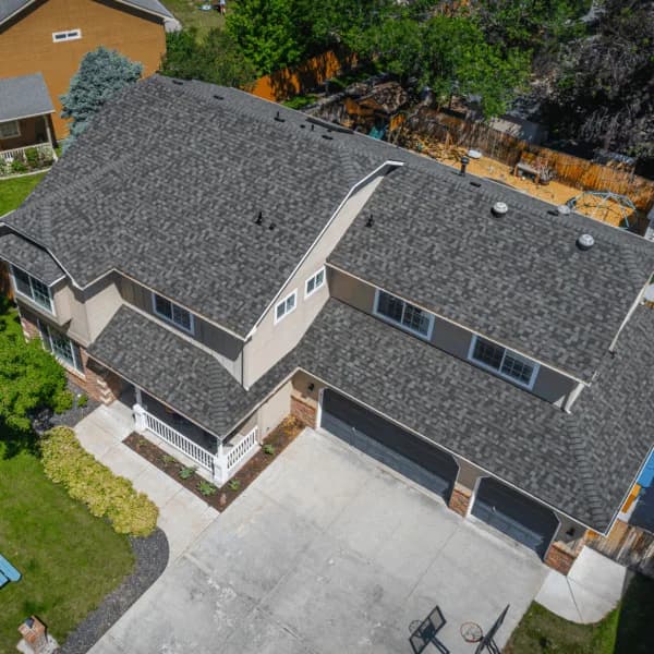 Aerial view of a tan two-story home with a bold, textured gray shingle roof and three-car black garage doors.