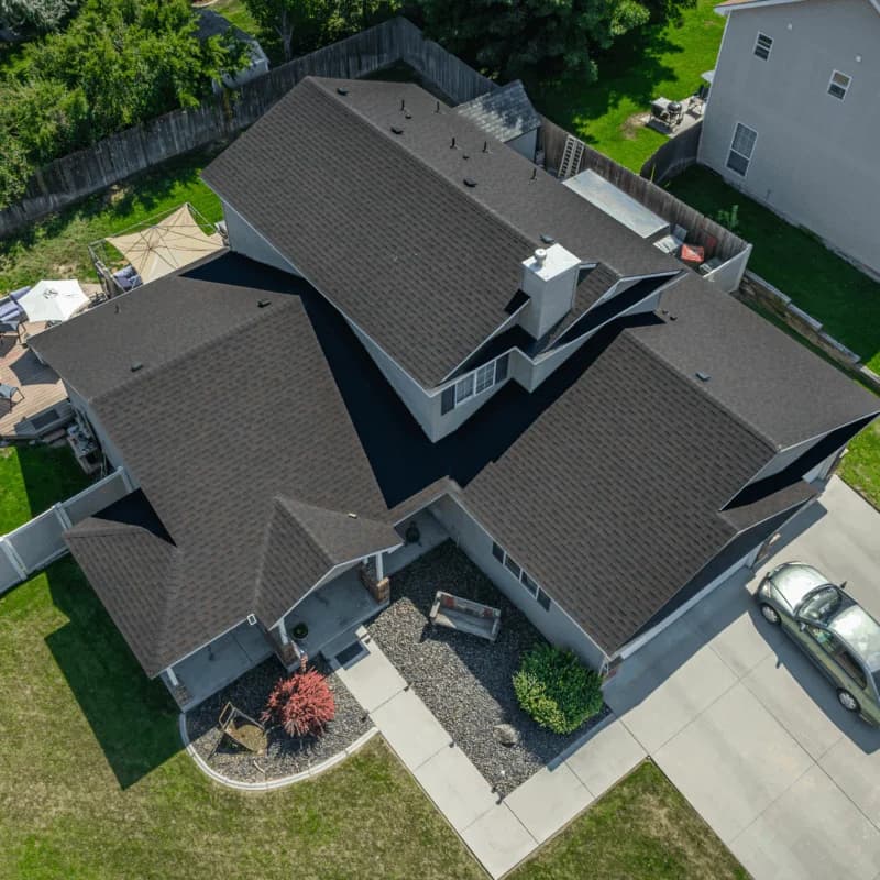 Overhead view of a large two-story home with a dark brown roof and tan siding, bordered by fencing and a tidy backyard.