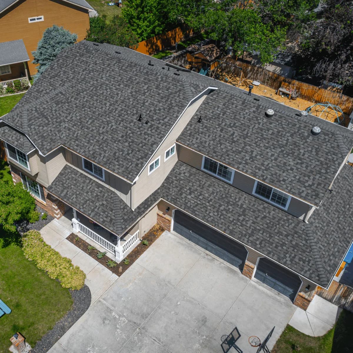 Aerial view of a tan two-story home with a bold, textured gray shingle roof and three-car black garage doors.