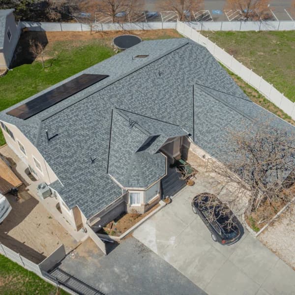 Aerial view of a beige two-story home with a light blue-gray shingle roof featuring solar panels and a small turret-style entry.