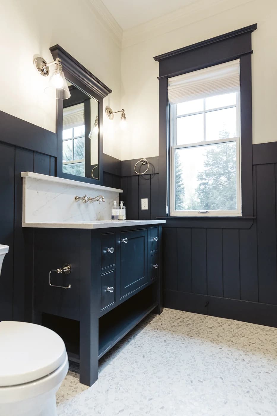 A modern bathroom featuring a black vanity with a white marble countertop and a built-in backsplash. The vanity includes multiple drawers with silver knobs and an open shelf beneath.