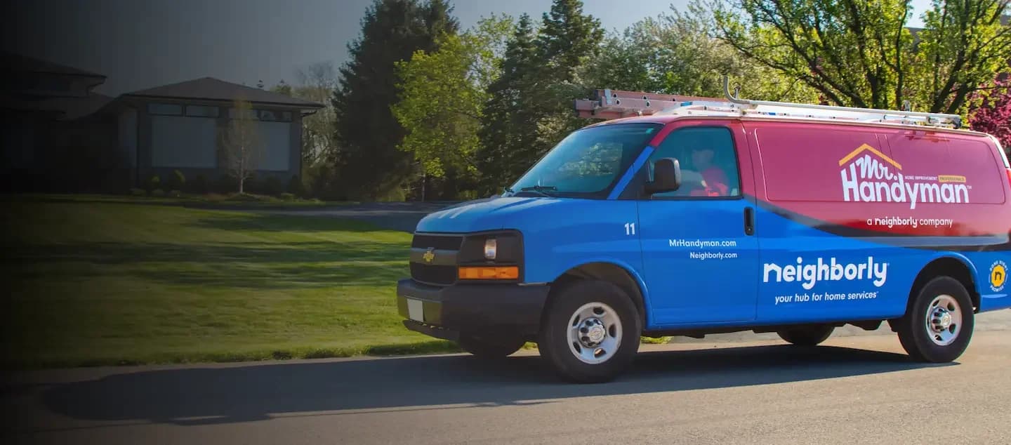 Mr. Handyman service van parked on a suburban street, with a ladder mounted on the roof and the Neighborly logo displayed on the side.