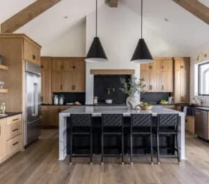 Modern kitchen with wood cabinets, large island with black chairs, and stainless steel appliances, showcasing available cabinetry at the Billings, MT location.