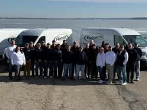 Robert's Plumbing team standing in front of work vans parked next to a lake in Madison, Wi. Team is posing together