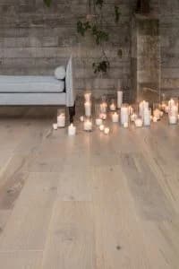 light hue of a hardwood floor. there are many candles on the floor that are lit next to a gray couch