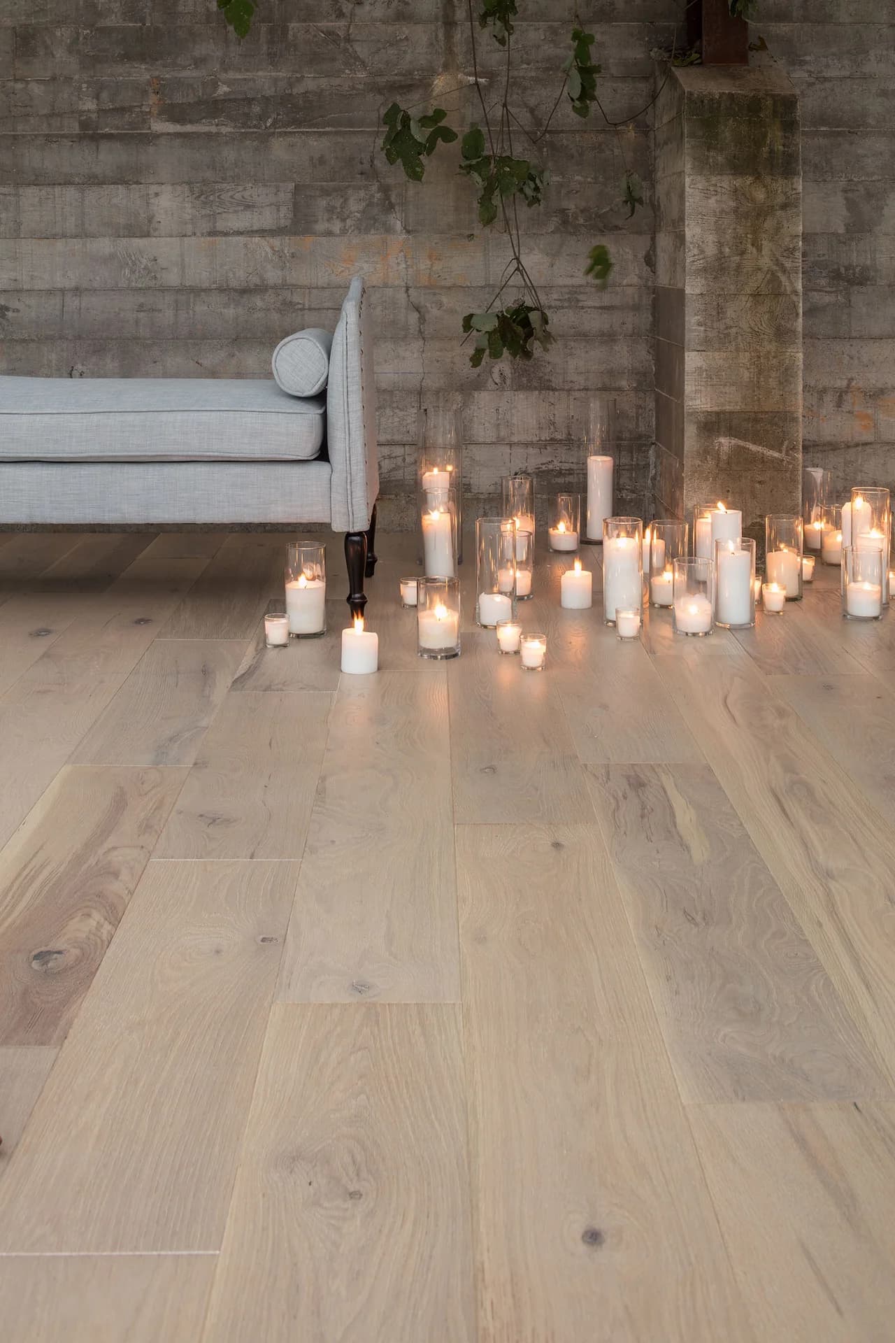 light hue of a hardwood floor. there are many candles on the floor that are lit next to a gray couch