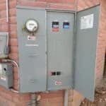 Electrical box mounted on a brick wall, with an open panel showing switches and a visible electricity meter.