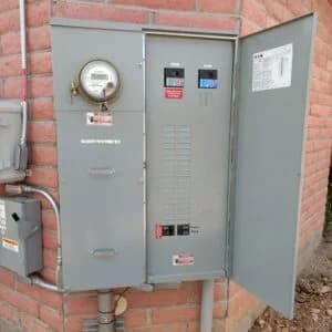 Electrical box mounted on a brick wall, with an open panel showing switches and a visible electricity meter.