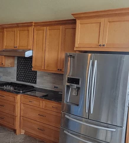 Custom kitchen cabinetry with wooden cabinets, modern stainless steel refrigerator, and gas stove, showcasing Ace Kustoms' craftsmanship and design expertise in home remodeling.