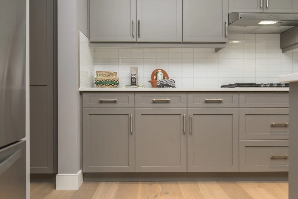 Modern kitchen featuring custom gray cabinetry, solid surface countertops, and stylish under-cabinet lighting, emphasizing functionality and aesthetics.