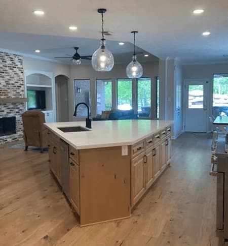 Modern kitchen with custom cabinetry, large island, quartz countertop, pendant lighting, and open layout connecting to living area and outdoor space.