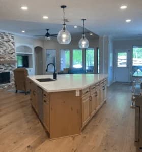 Modern kitchen with custom cabinetry, large island, quartz countertop, pendant lighting, and open layout connecting to living area and outdoor space.