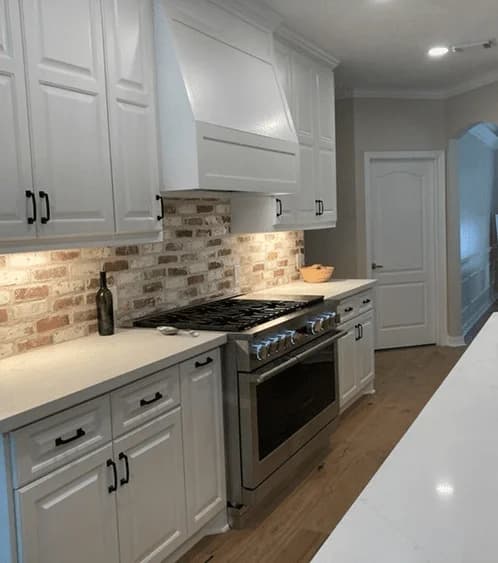 Modern kitchen featuring white cabinetry, stainless steel appliances, and a brick backsplash, showcasing custom woodworking craftsmanship by Ace Kustoms Cabinets & Trim.