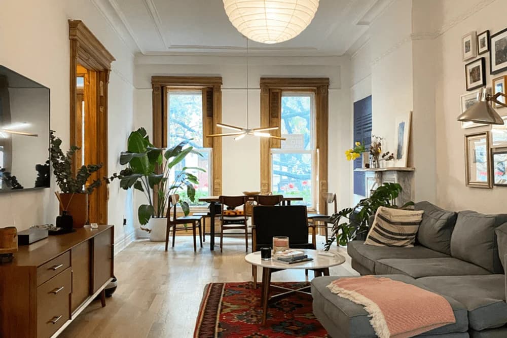Modern living room with stylish furniture, under-cabinet lighting, large windows, and plants, showcasing a blend of comfort and elegance for enhanced interior ambiance.