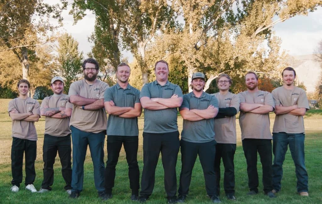 Team photo of Night Vision Lighting & Electric crew standing outdoors with arms crossed, smiling in uniform shirts,