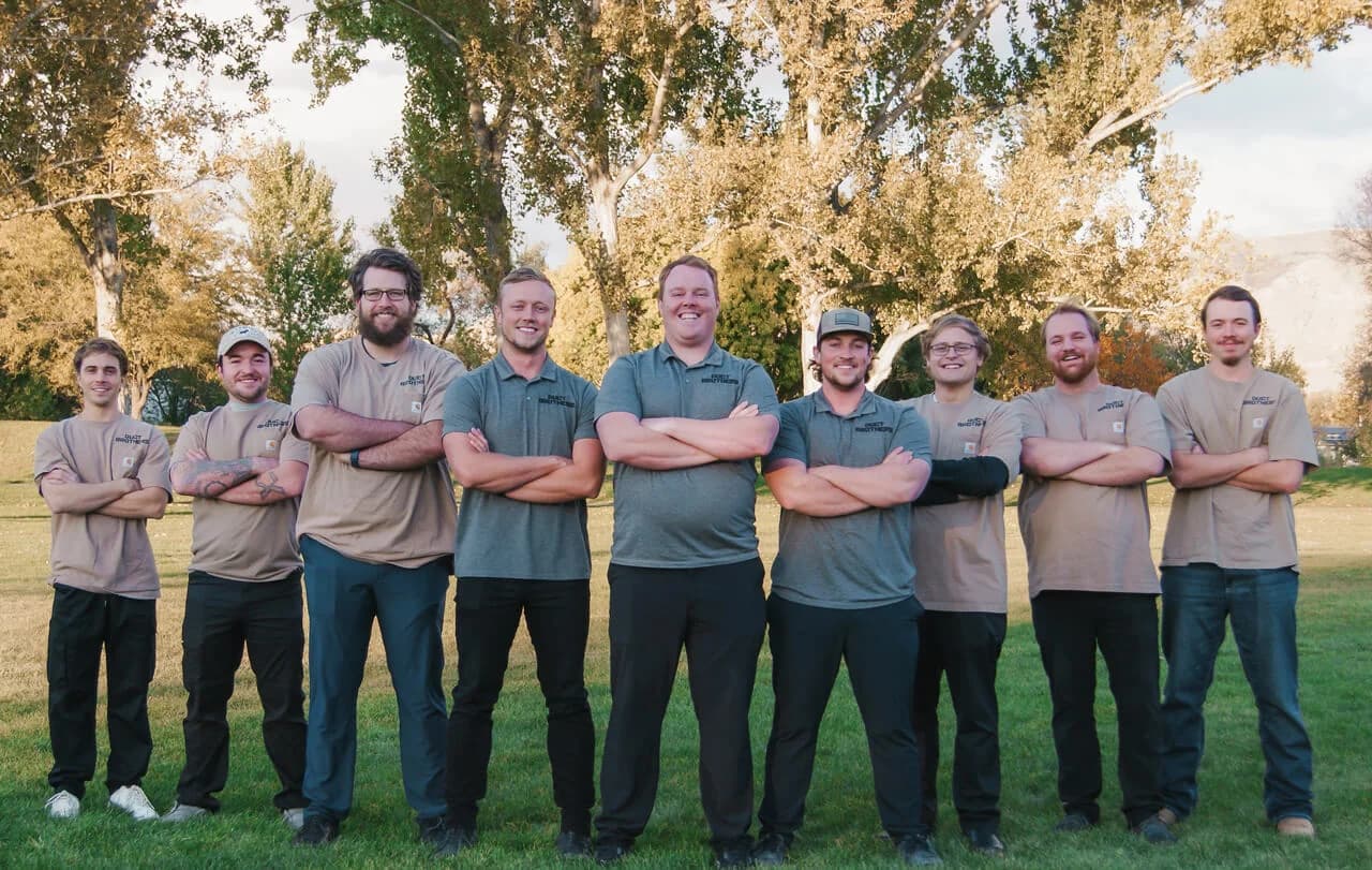 Team photo of Night Vision Lighting & Electric crew standing outdoors with arms crossed, smiling in uniform shirts,