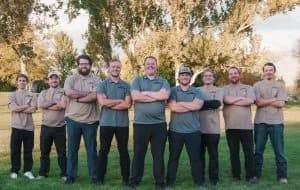 Team photo of Night Vision Lighting & Electric crew standing outdoors with arms crossed, smiling in uniform shirts,