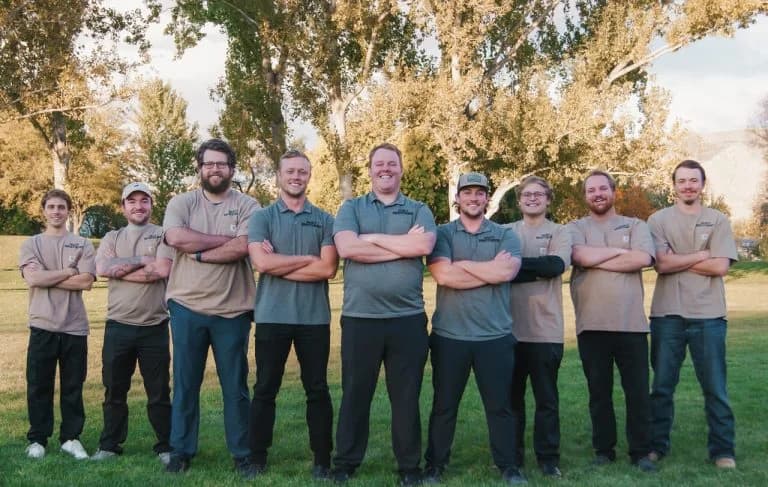Team photo of Night Vision Lighting & Electric crew standing outdoors with arms crossed, smiling in uniform shirts,