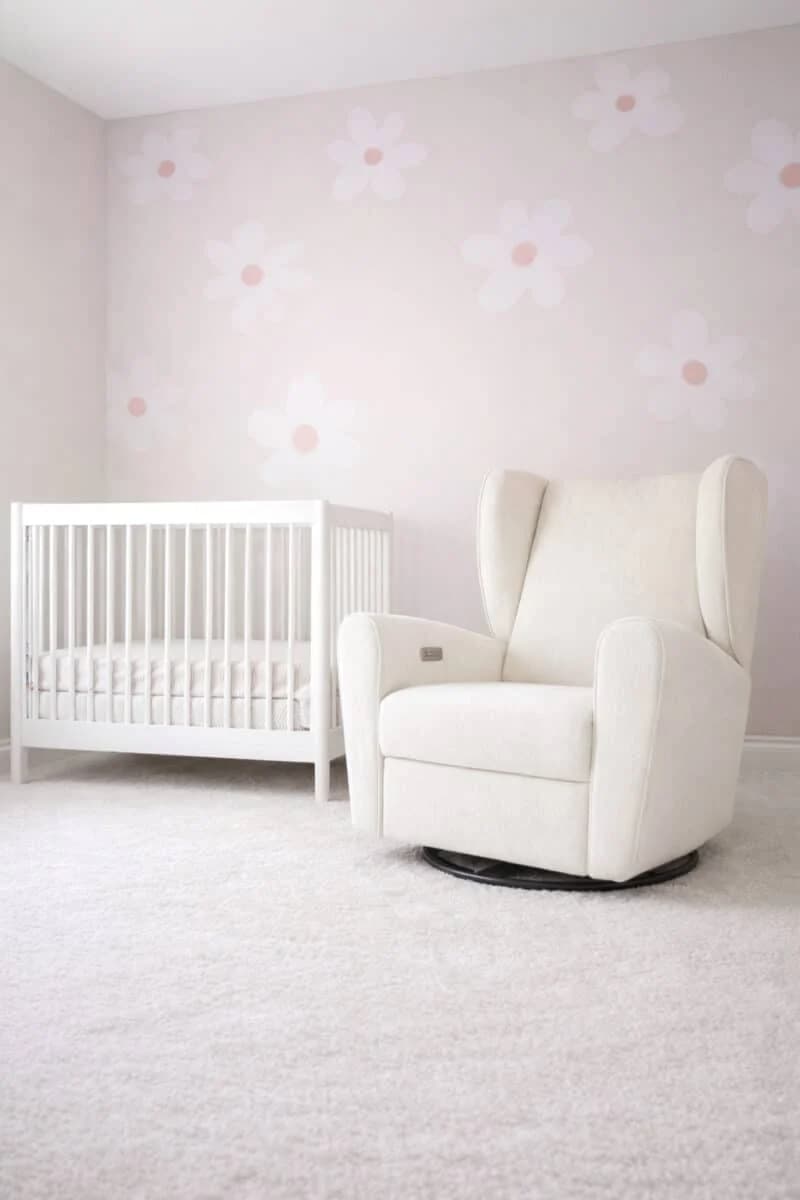 A cozy and bright nursery room with a white crib, cream rocking chair, and delicate floral wallpaper.