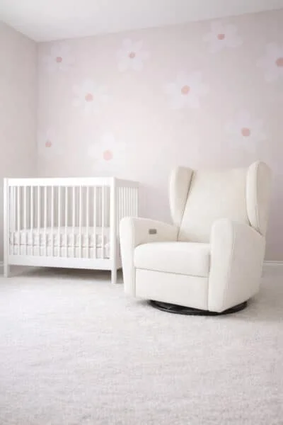 A cozy and bright nursery room with a white crib, cream rocking chair, and delicate floral wallpaper.