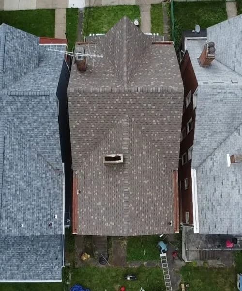 Aerial view of a completed residential roof installation with asphalt shingles, showcasing quality craftsmanship by Alan Construction, surrounded by neighboring houses in a Pittsburgh neighborhood.
