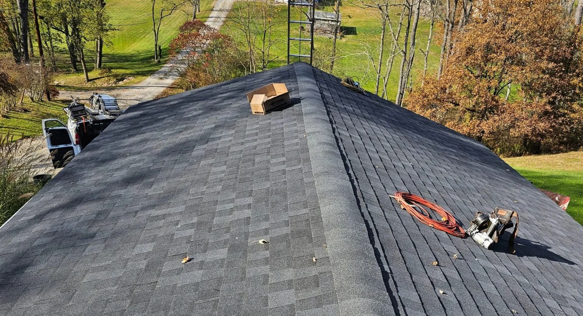 Newly installed asphalt shingle roof with tools and equipment on a residential home, surrounded by trees and a clear pathway, illustrating roofing maintenance and installation quality.