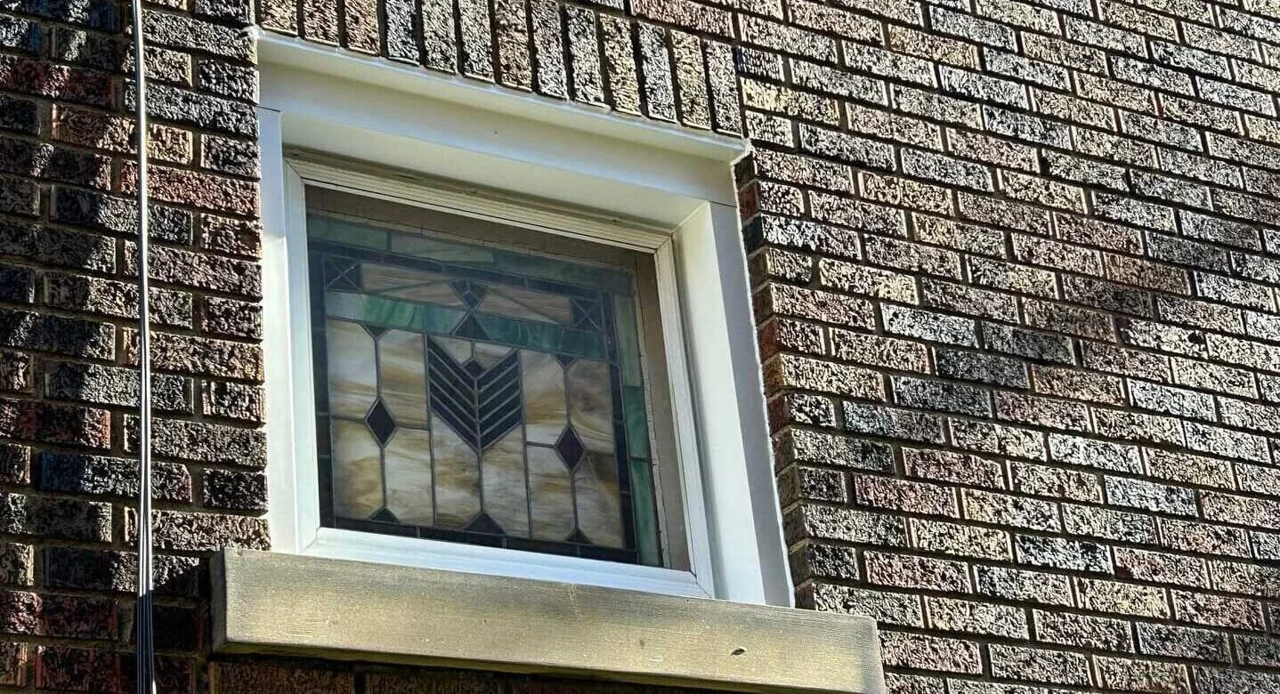 Stained glass window framed by new window wrap flashing on brick exterior, showcasing meticulous installation for weatherproofing.