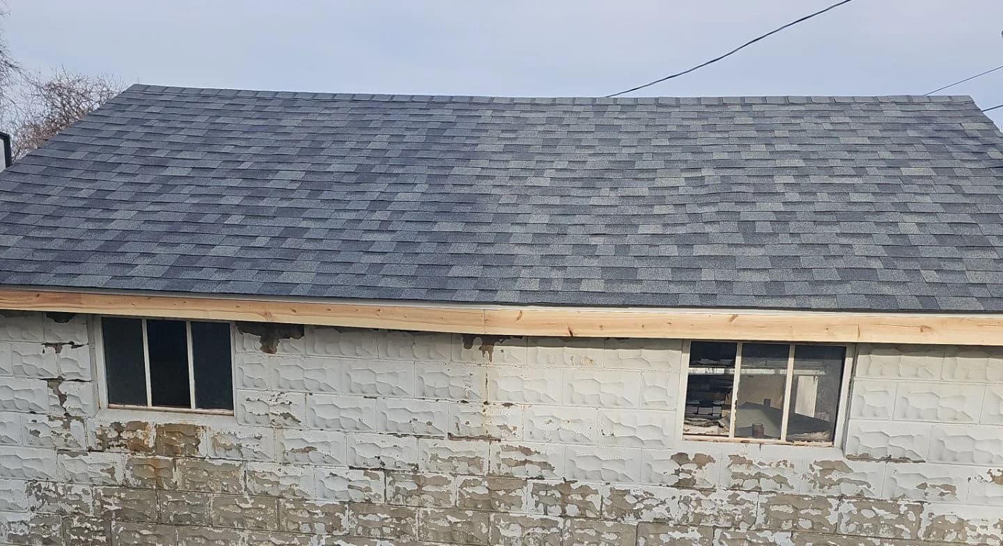 Garage roof replacement showcasing new asphalt shingles and partially visible windows on a renovated structure.