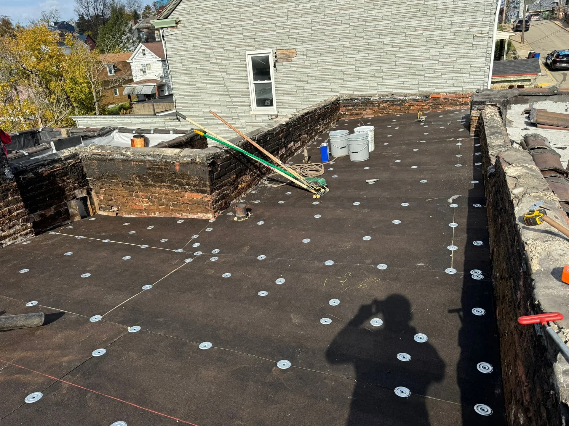 Rubber roof installation on South Side property, featuring a flat deck with fiber board and EPDM roofing materials, tools, and containers visible.