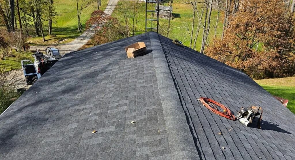 Newly installed asphalt shingle roof with tools and equipment on a residential home, surrounded by trees and a clear pathway, illustrating roofing maintenance and installation quality.