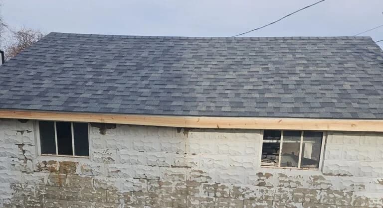 Garage roof replacement showcasing new asphalt shingles and partially visible windows on a renovated structure.