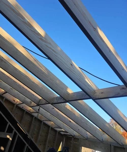 Wooden rafters under construction, showcasing a clear blue sky above, illustrating the roofing process for residential buildings by Alan Construction.
