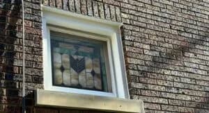 Stained glass window framed by new window wrap flashing on brick exterior, showcasing meticulous installation for weatherproofing.