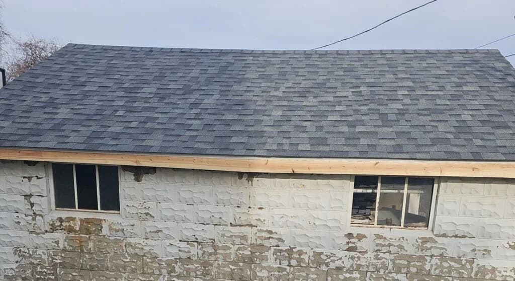 Garage roof replacement showcasing new asphalt shingles and partially visible windows on a renovated structure.