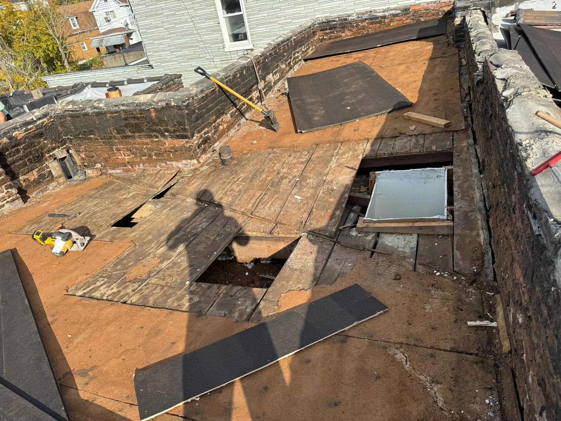 Roof deck with removed wooden boards, exposed areas for inspection and repair, tools including a saw, and preparation for rubber roofing installation at a South Side property.