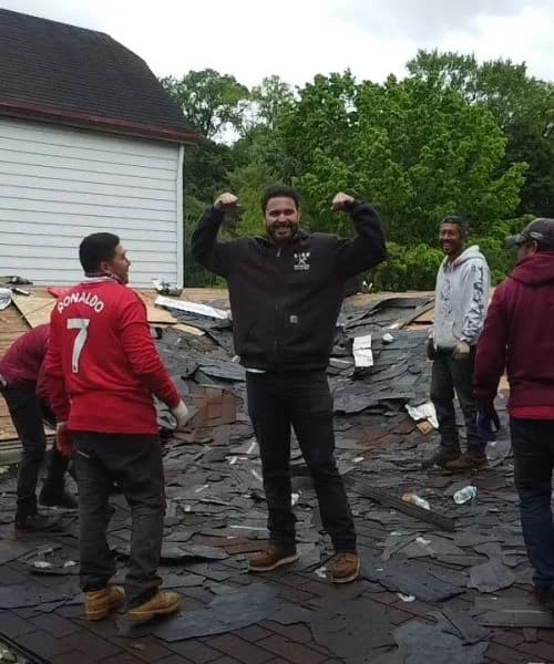 Team of roofers working on a residential roof replacement, showcasing camaraderie and teamwork, with one man celebrating and others assisting in the background.