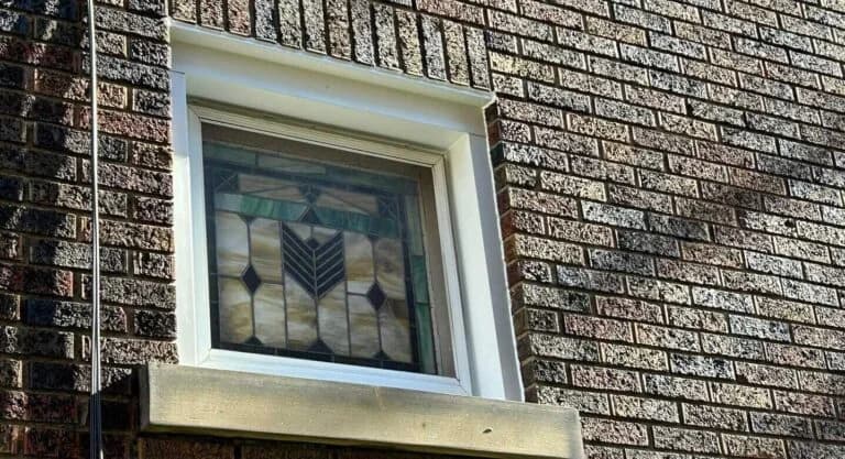 Stained glass window framed by new window wrap flashing on brick exterior, showcasing meticulous installation for weatherproofing.
