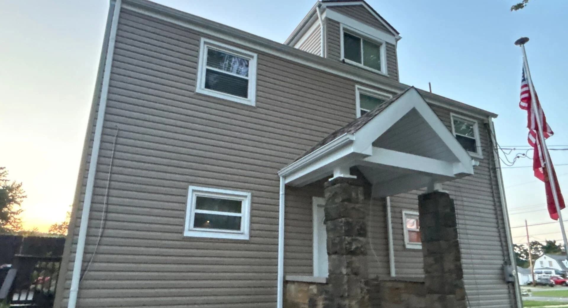 Siding replacement on residential building with stone accents and American flags, showcasing Alan Construction LLC's exterior services in Pittsburgh.