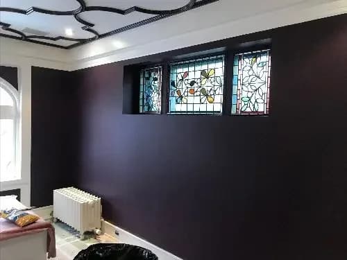 A room with dark and deep purple walls, renovated ceiling with an interesting design and stained glass windows.
