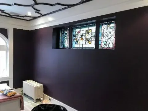 A room with dark and deep purple walls, renovated ceiling with an interesting design and stained glass windows.