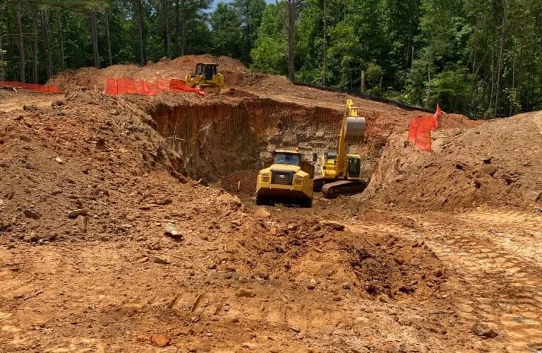 Deep excavation for site preparation with heavy equipment and land grading.